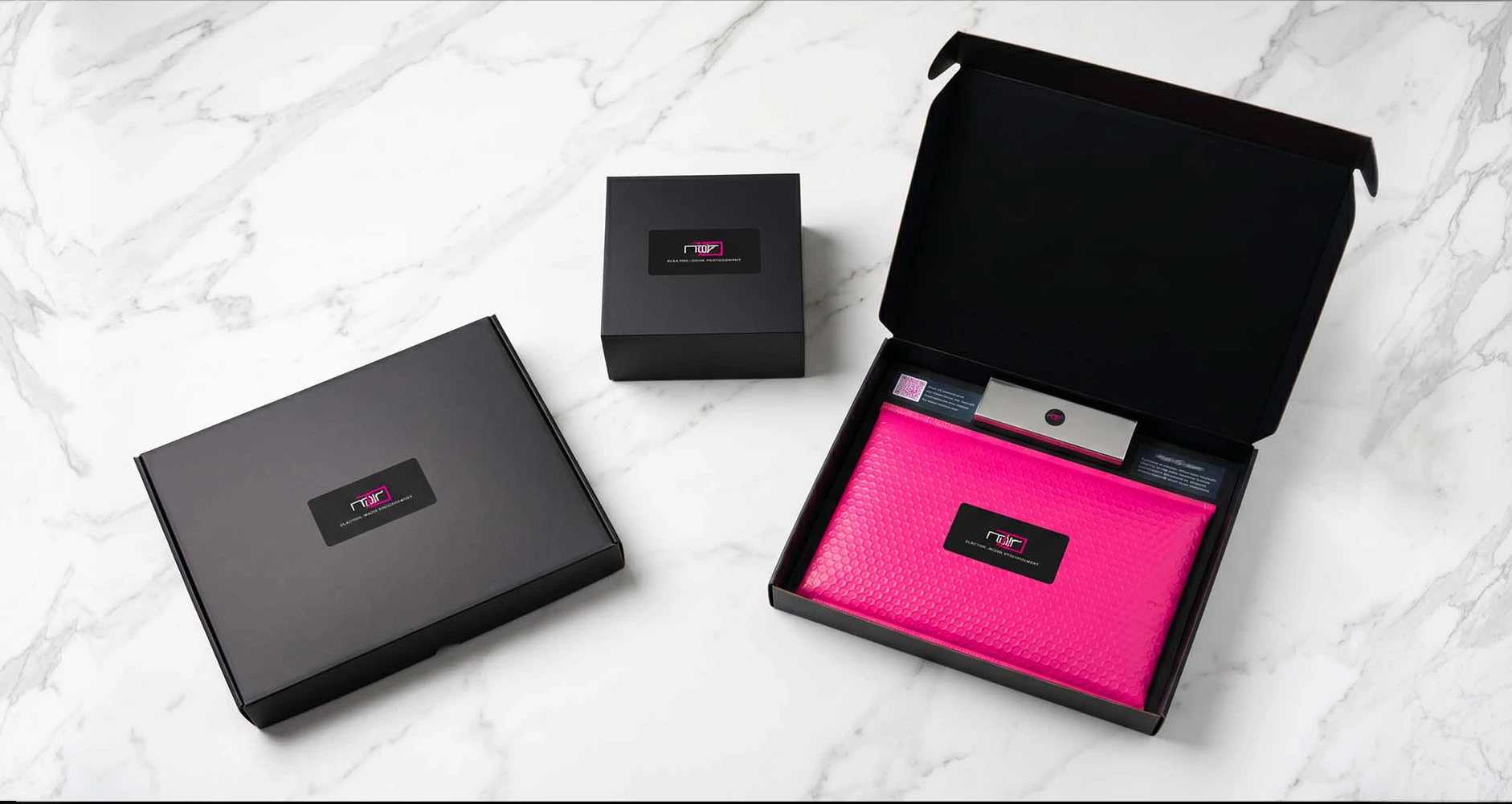 Noir10 Package design - black boxes and neon pink padding